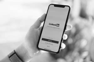 A black and white image of a person holding a smartphone with the linkedin login page displayed on the screen. the text on the phone reads "connect to opportunity.