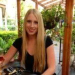 Woman with long blonde hair sitting at an outdoor restaurant table.