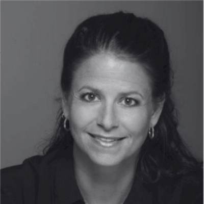 Woman smiling, wearing a dark top, with hoop earrings, in a black and white portrait.