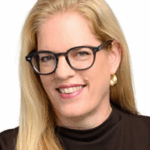 Woman with long blonde hair, glasses, gold earring, and a black top, smiling at camera.