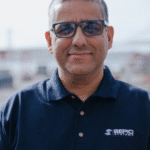 Man in glasses wearing a navy Sepio Systems polo shirt, standing outdoors and smiling.