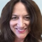 Woman with long brown hair smiling at the camera against a light blue background.