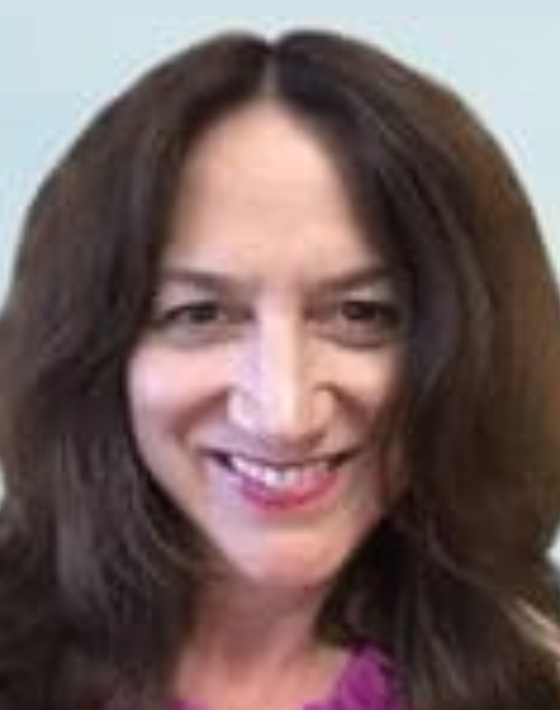 Woman with long brown hair smiling at the camera against a light blue background.
