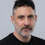 Man with short dark hair and beard wearing a black sweater, facing the camera.