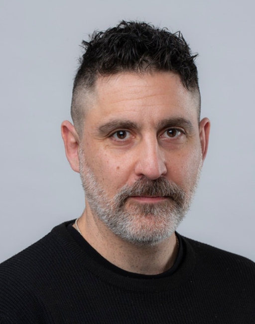 Man with short dark hair and beard wearing a black sweater, facing the camera.