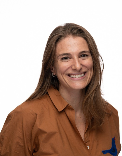 Woman with long brown hair smiling, wearing a brown shirt, on a white background.