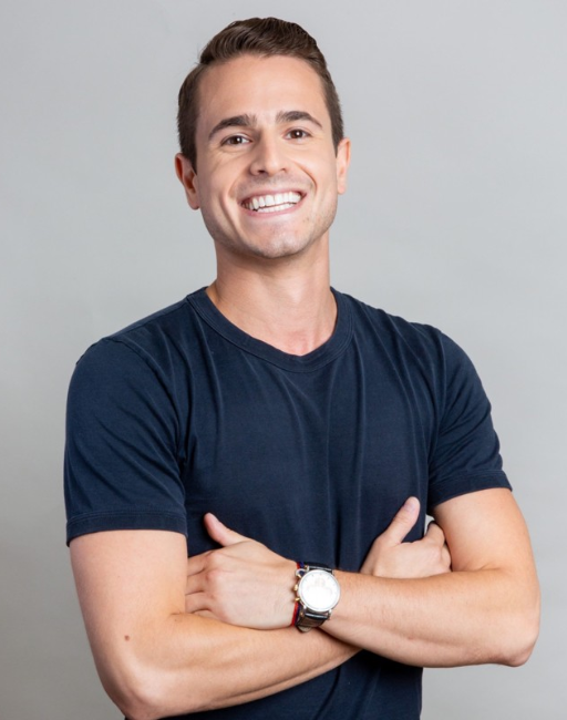 Smiling man in a navy t-shirt with arms crossed, standing against a light gray background.