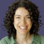 Smiling woman with curly hair wearing a green shirt on a solid purple background.