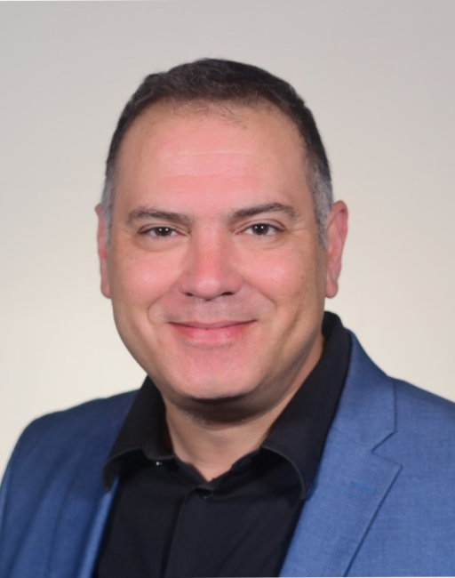 Smiling man in a blue blazer and black shirt against a plain light background.